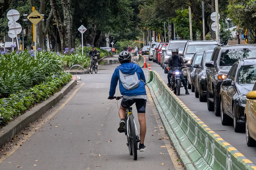 Un ciclista avanza por la ciclorruta separada del tráfico, junto a una fila de carros y motos detenidos